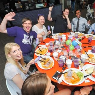 一群TCU学生在欢乐的圆桌旁举起紫色玛格丽塔酒庆祝