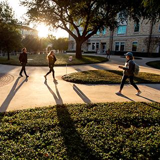 在阳光明媚的日子里，身着夹克的TCU学生走在校园里，投下长长的影子